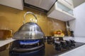 Shiny stainless tea kettle teapot with boiling water on burning gas stove on modern kitchen yellow interior background