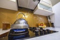 Shiny stainless tea kettle teapot with boiling water on burning gas stove on modern kitchen yellow interior background