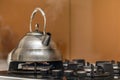 Shiny stainless tea kettle teapot with boiling water on gas stove on kitchen yellow copy space background