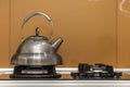 Shiny stainless tea kettle teapot with boiling water on gas stove on kitchen yellow copy space background