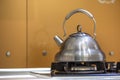 Shiny stainless tea kettle teapot with boiling water on gas stove on kitchen yellow copy space background