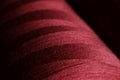 Shiny surface of a bobbin with neat wound deep red thread in dark scenery