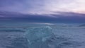 Shiny turquoise transparent ice floe on the snow-covered surface of a frozen lake. Royalty Free Stock Photo