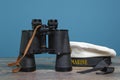 Ship binoculars and peakless cap on a turquoise background on a textured wooden table