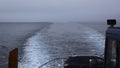 Ship with car sails into sea in cloudy weather. Clip. Sailing on ferry with car in sea. View of line left by sailing