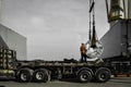 Ship crane put away steel coil on the trailer, worker stands on truck placing coil on the support skit.