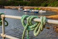 Ship mooring rope around the railings in the harbor on the pier, boats on the sea water in the background Royalty Free Stock Photo