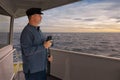A ship`s captain with binoculars stands on the bridge and looks out to sea.