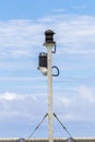 Ship`s stern light post with two lights against cloudy blue sky. Turnbuckles and steel wires are holding the pole upright