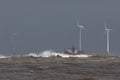 Ship sailing in rough sea around offshore wind farm turbines Royalty Free Stock Photo