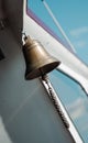 Vintage brass ship's bell hanging on a wall, with a textured rope pull, against a bright blue sky, evoking maritime Royalty Free Stock Photo