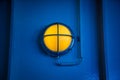 Ship yellow deck lamp bulkhead light surrounded by a metal rusted frame fixed to a painted light blue wall