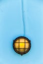Ship yellow bulkhead light deck lamp surrounded by a blue metal rusted frame Royalty Free Stock Photo