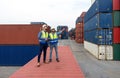 Shipment worker use a walkietalkie to point to container storage location, explain to colleague about planning for next shipment.