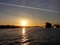 Shipping boat pulled by tugboats out of harbor as Shipping boat is unloaded by cranes in Oakland Harbor at sunset