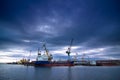 Shipping vessels and port cranes line the dock at sunset. Industrial maritime freight terminal, global trade gateway