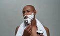 Shirtless attractive young african american man looking at camera, using brush while applying shaving foam on his face Royalty Free Stock Photo