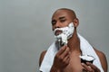 Shirtless attractive young african american man looking at camera, using brush while applying shaving foam on his face Royalty Free Stock Photo