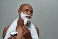 Shirtless attractive young african american man smiling at camera, using brush while applying shaving foam on his face Royalty Free Stock Photo