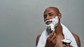 Shirtless attractive young african american man smiling at camera, using brush while applying shaving foam on his face Royalty Free Stock Photo