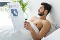 shirtless bearded man reading business newspaper in bed