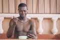 Shirtless black man enjoying a bowl of cereal while listening to music and smiling at his phone Royalty Free Stock Photo