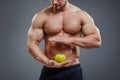 Shirtless bodybuilder holding an apple in his hands.