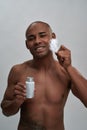 Shirtless handsome african american guy smiling, holding aftershave lotion, touching his facial skin with feather Royalty Free Stock Photo