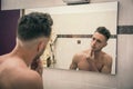 Shirtless young man examining his face in bathroom mirror Royalty Free Stock Photo