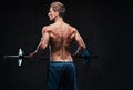 Shirtless male holds barbell over dark grey background.