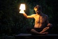 Shirtless man looking for something in the darkness outdoor, bright lamp in his hand