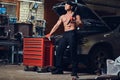 Shirtless mechanic in a garage.