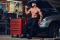 Shirtless mechanic in a garage.