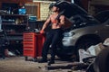 Shirtless mechanic in a garage.