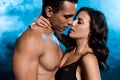 shirtless mixed race man kissing young attractive woman on blue with smoke.