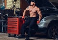 Shirtless mechanic in a garage.