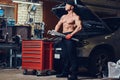 Shirtless mechanic in a garage.