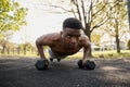 Shirtless young black man with wireless earphones doing push-ups with dumbbells in park Royalty Free Stock Photo