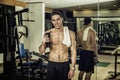 Shirtless young man holding protein shake in gym