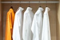 Shirts hang in a walking closet with glass door. One of those is in orange standout from others that are in white