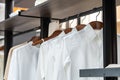 Shirts hang in a walking closet wiht beige and white T shirt on it