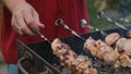 Shish kebab grilling, barbecue preparation. Hands cooking meat skewers outdoors.