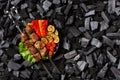 Shish kebab on skewers and grilled sweet pepper, zucchini, cherry, tomato on a round plate. Charcoal background. Royalty Free Stock Photo