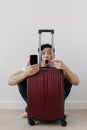 Shock and surprise face of man using mobile phone application for travel, sitting with his baggage or luggage. Royalty Free Stock Photo