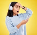 Shock, surprise and woman with phone, headphones and hand on head isolated on yellow background. Social media, music