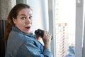 Shocked adult woman after spying out the window with binoculars, domestic room Royalty Free Stock Photo