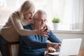 Shocked aged couple surprised by news at laptop online