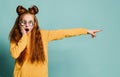 Shocked and amazed teen girl with long vivid red hair in fashion round glasses and yellow sweatshirt is pointing aside Royalty Free Stock Photo