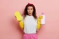 Shocked and amazed young housewife, stands in shock pose, realising amount of work to do, holds a sponge and a bottle