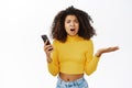 Shocked, angry african american girl, reacts on smth frustrating on mobile phone, complaining on smartphone text